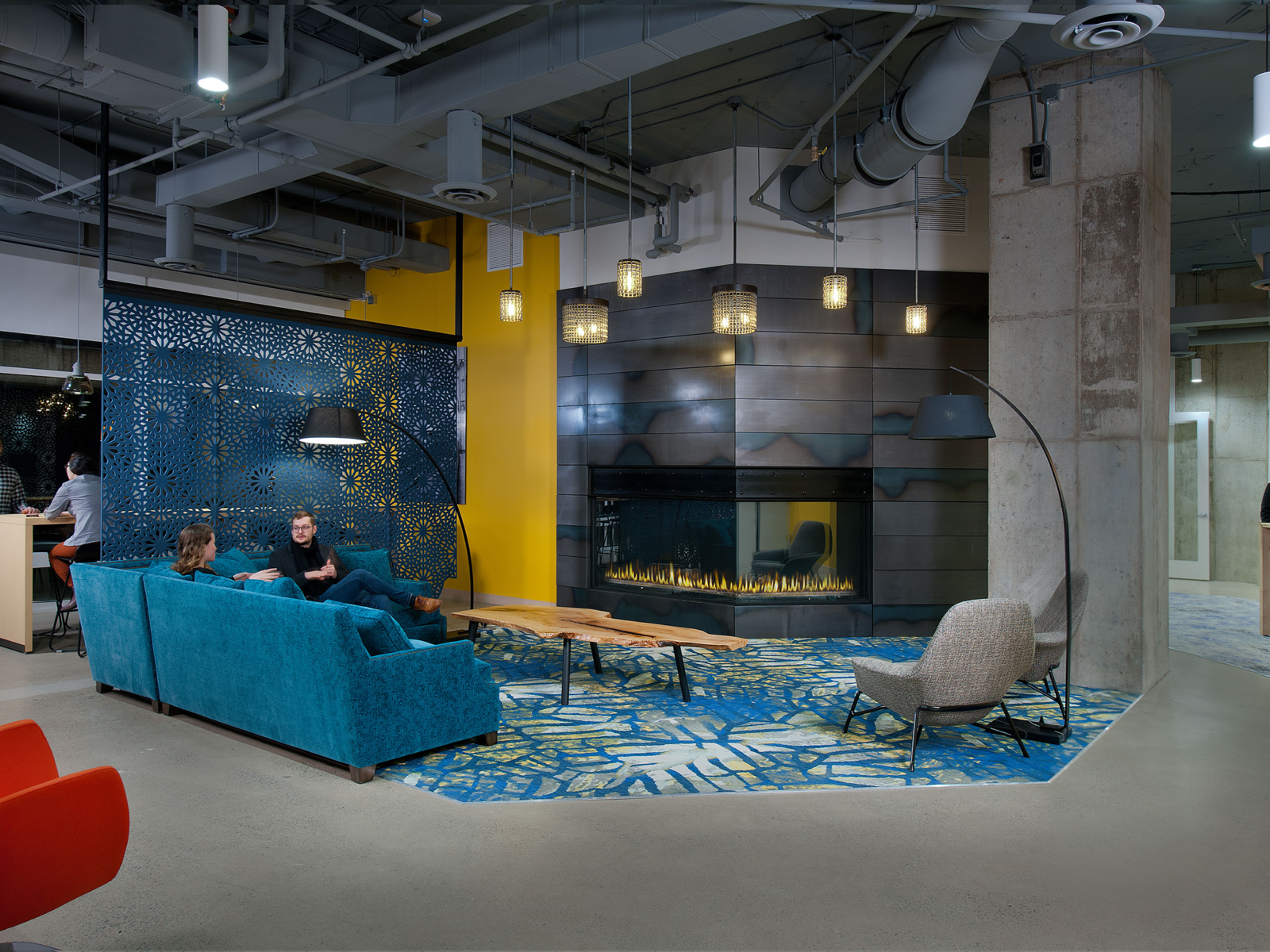 communal space with blue carpeting creating a cozy zone around a fireplace